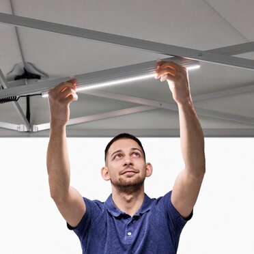 The man attaches the LED strips to the folding gazebo.